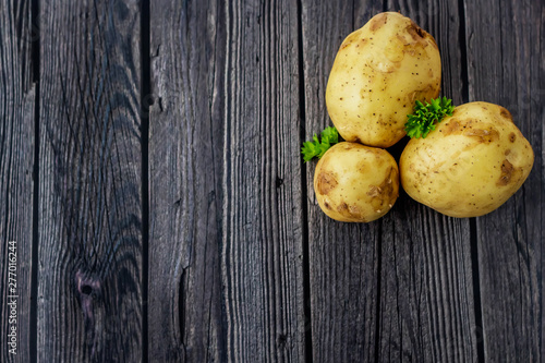 Young raw unpeeled potatoes and bunch greens on wooden dark background. Harvest. Flat lay composition. Layout with copy space for text .