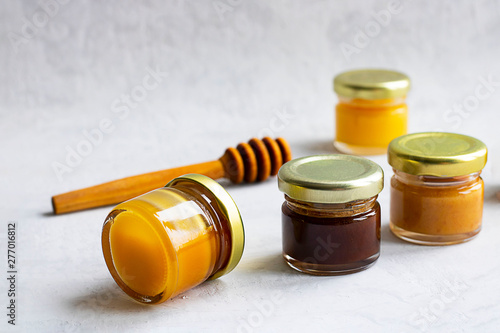 Four Small glass jar with metal cap with different kinds and colours of honey put in line and wooden spoon isolate and on grey cement background Healthy product, natural. Horizontal
