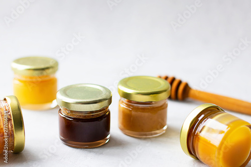 Five Small glass jar with metal cap with different kinds and colours of honey put in line and wooden spoon isolate and on grey cement background with copy space. Healthy product, natural. Horizontal