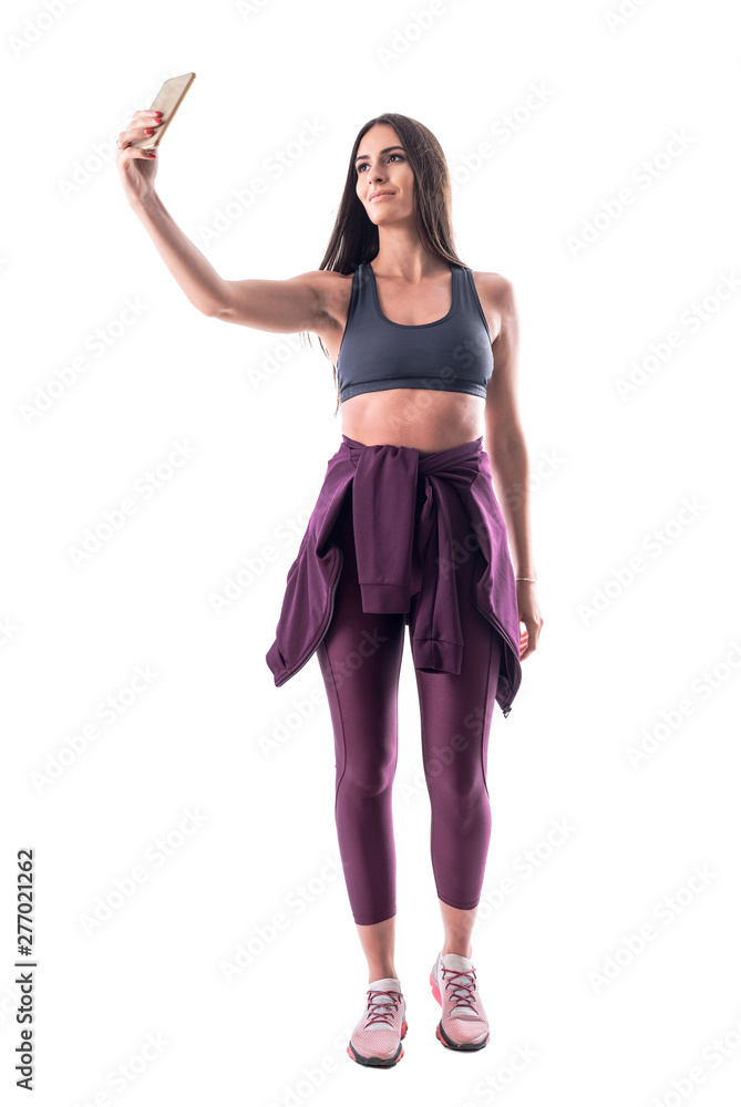 Attractive fitness model female athlete taking selfie with cellphone. Full body isolated on white background. Attractive fitness model female athlete taking selfie with cellphone. Full body isolated on white background.