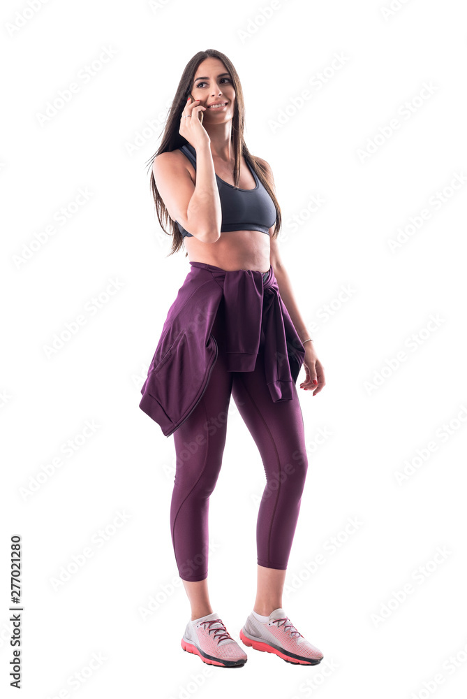 Happy relaxed fitness woman in sportswear talking on the cellphone looking back over shoulder. Full body isolated on white background. Happy relaxed fitness woman in sportswear talking on the cellphone looking back over shoulder. Full body isolated on white background.
