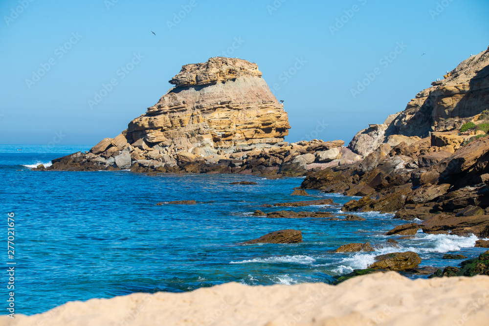 Stones and rocks on a beach under sky blue Atlantic Ocean against the cliffs during sunny day