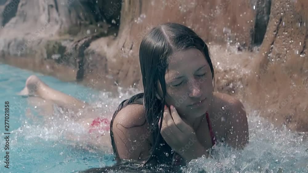 tanned lady in red swimsuit rests under artificial waterfall and straightens long dark wet hair close view slow motion tanned lady in red swimsuit rests under artificial waterfall and straightens long dark wet hair close view slow motion