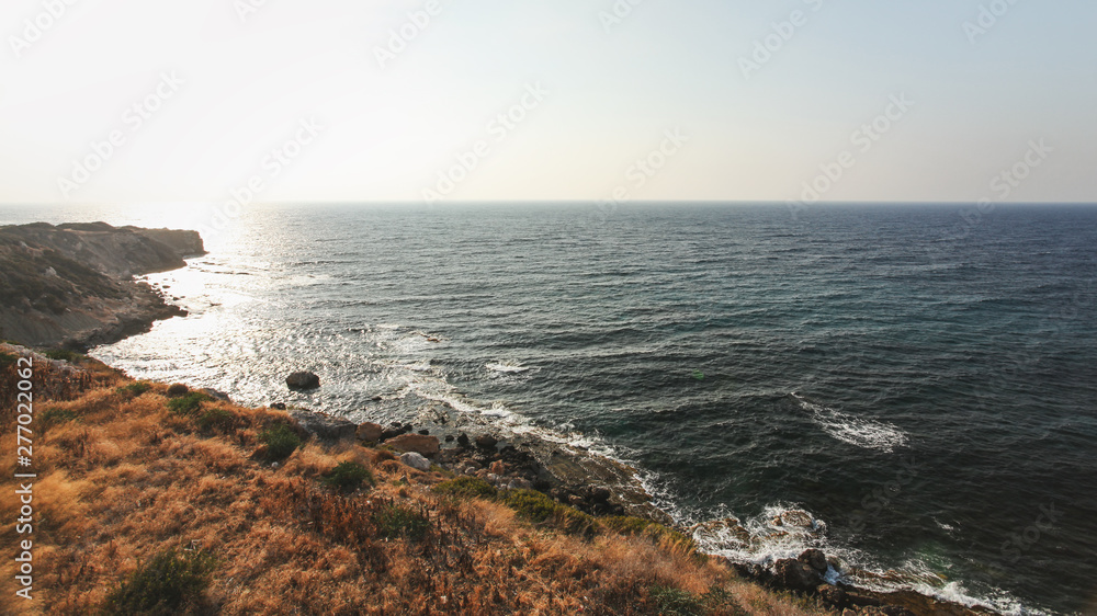 Afternoon sun shines on rough coast with rocky cliffs and deep sea in Karpass region of Northern Cyprus