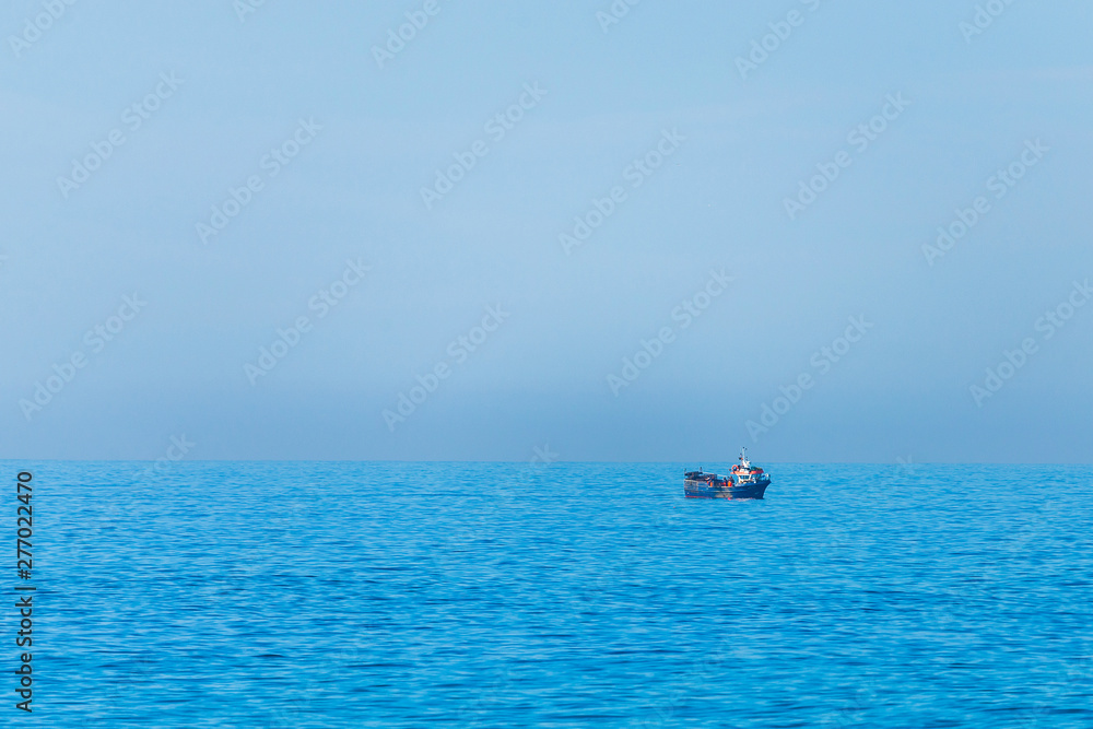 Minimalistic image of the sea with a fishing boat. Blue sea water and clear sky.