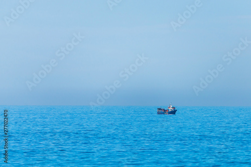Minimalistic image of the sea with a fishing boat. Blue sea water and clear sky. © rostovdriver