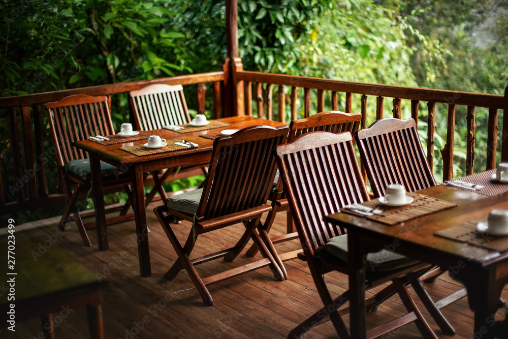 Empty wooden chairs and tables, with coffee cups upside down - ready for morning breakfast, jungle rainforest in background
