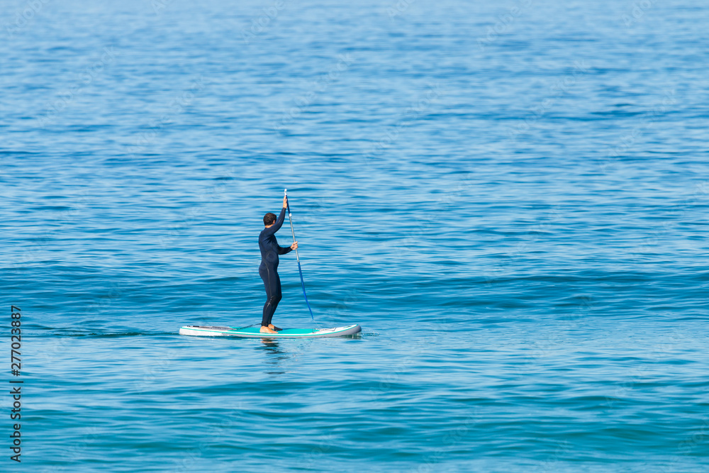 Stand up paddle boarder in wetsuit paddling on a sea. Minimalist image