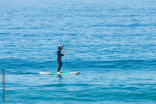 Obraz na płótnie Stand up paddle boarder in wetsuit paddling on a sea. Minimalist image w salonie
