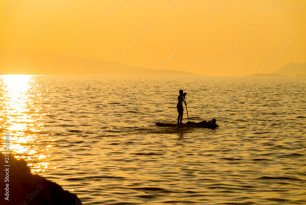 Silhouette of young couple on stand up paddle board. Active vacation, beach life.
