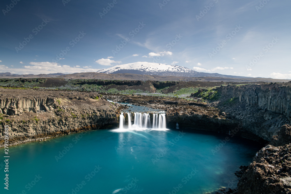 Scenic wide angle view of Thjofafoss waterfall and Hekla mountain on the background covered by snow Scenic wide angle view of Thjofafoss waterfall and Hekla mountain on the background covered by snow