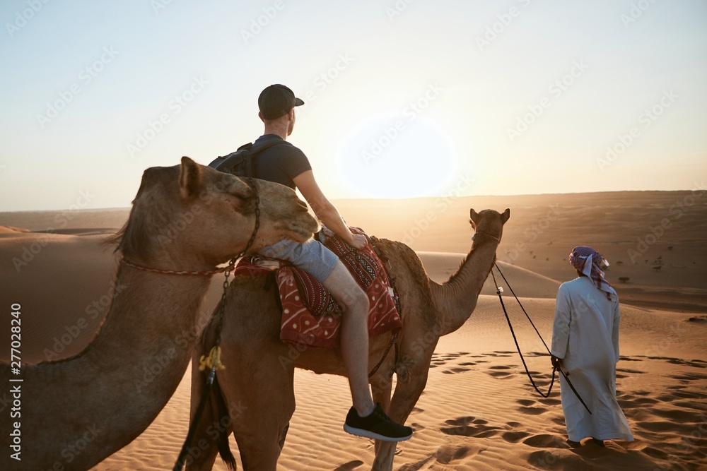 Fotografie Camel riding in desert at sunset