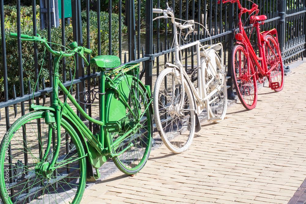 Three colorful bikes - green, white and red - are on the dutch street in the sunlight