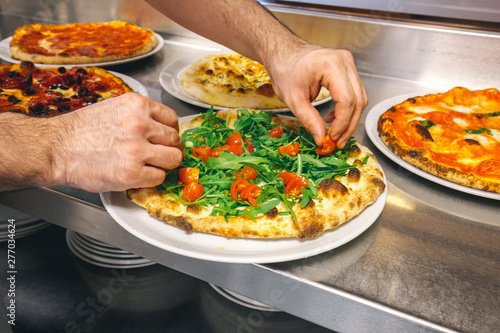 Preparing italian pizza with Parmigiano cheese tomato garnished with fresh vegetables and basil and rocket leaves.