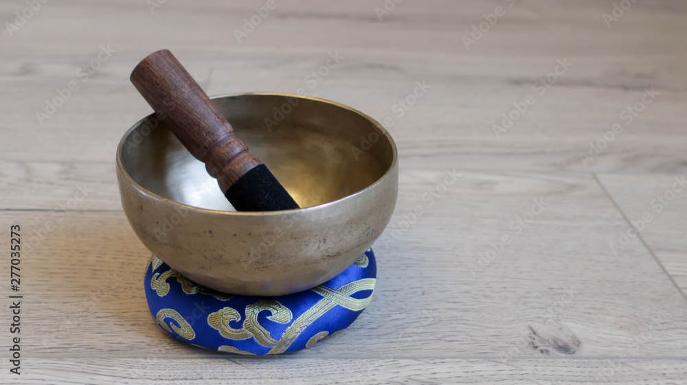 Handmade singing bowl stands on a wooden floor.