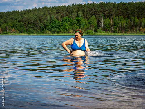 Mature woman in blue swimsuit comes out of the water