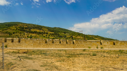 View of the western wall of the Naryn-Kala fortress and adjacent territories. This is a mountainous area covered with vegetation, partly used for agriculture.