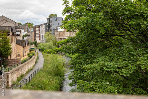 view down a bridge in Stockbridge, Edinburgh to the Water of Leith, with lush trees and a pathway
