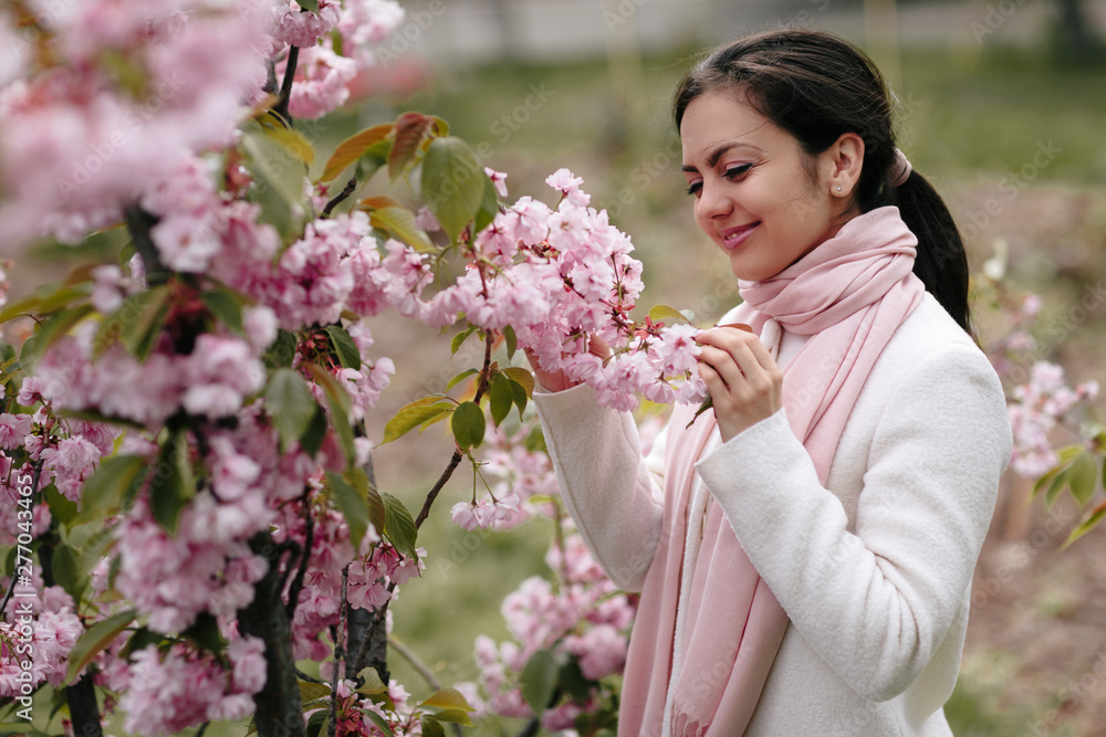 Beautiful young brunette woman enjoying spring day in park during Sakura cherry blossom season Beautiful young brunette woman enjoying spring day in park during Sakura cherry blossom season