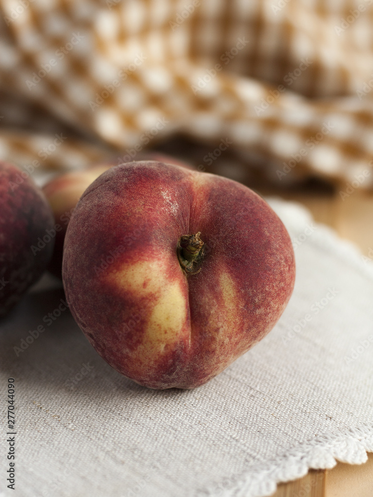 One peache on a linen cloth with an orange checkered napkin on a background. One peache on a linen cloth with an orange checkered napkin on a background.