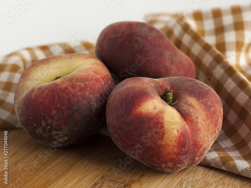 Three peaches on a wooden board with an orange checkered napkin on a background. Close.