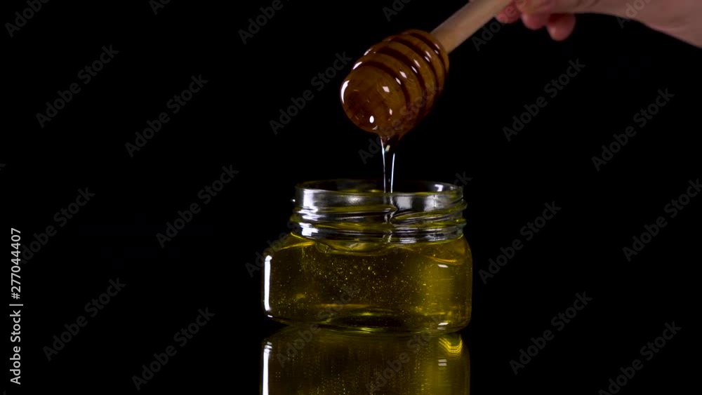 Honey dripping from honey dipper on black background. Healthy organic Thick honey dipping from the wooden honey spoon. Honey dripping from honey dipper on black background. Healthy organic Thick honey dipping from the wooden honey spoon.