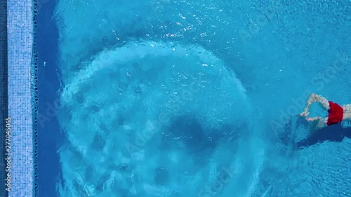 View from the top as a man stands on the edge of the pool, dives and swims under the water