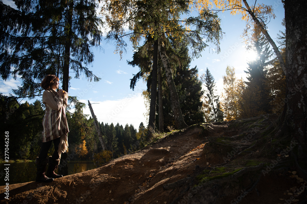The girl climbs the mountain in the autumn forest near the lake towards the sun in brown clothes with a beige wool blanket. The girl climbs the mountain in the autumn forest near the lake towards the sun in brown clothes with a beige wool blanket.