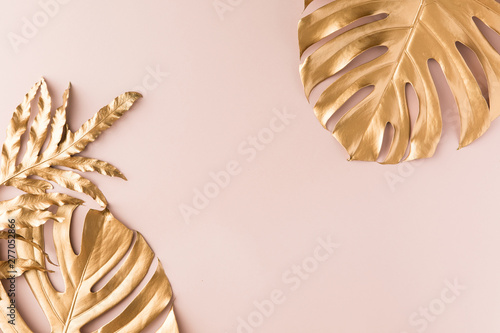 Flat lay of gold tropical palm leaves Monstera on pastel gold pink white background. Top view of minimal concept.