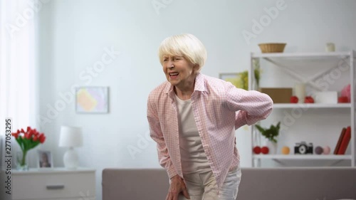 Old lady standing up from sofa suddenly feeling sharp lower back pain, spasm