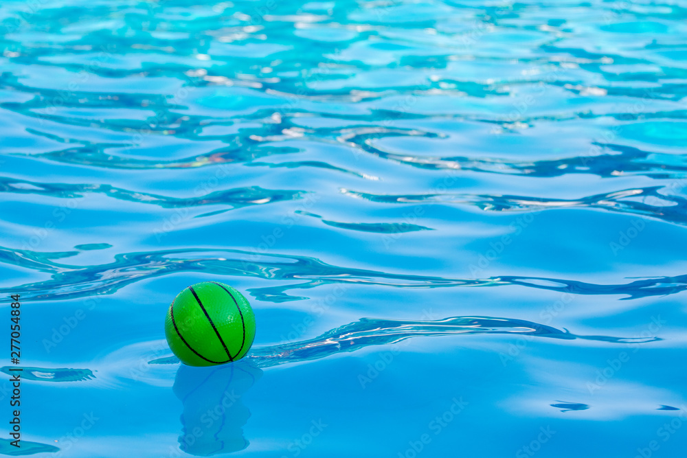 Green ball in the clear water of the pool. Summer vacation at sea_