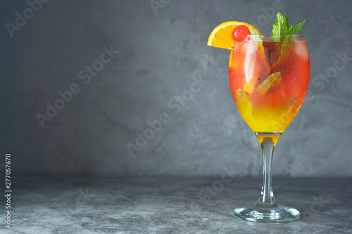 Summer cocktail. Orange juice with mint, syrop, fruit slices and cherry with ice. Dark background.