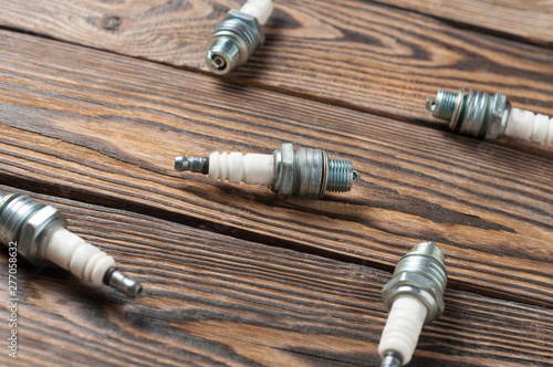 Five spark plugs for engine strewn on old brown wooden table in workshop