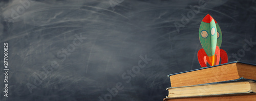 education and back to school concept. cardboard rocket over books in front of classroom blackboard