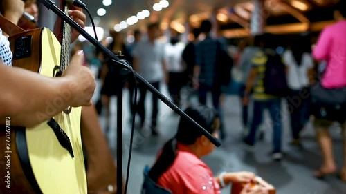 Thai street musicians playing guitar and sing song with blurry many people walking, Street musician playing a guitar during a performance at Sathorn skywalk , Bangkok, Thailand.