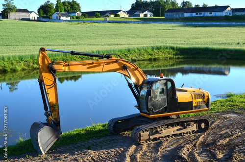 Excavator by the river against the green field of the countryside during the construction of the highway - Image photo