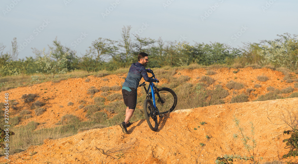 Cyclist in shorts and jersey on a modern carbon hardtail bike with an air suspension fork rides off-road on the orange-red hills at sunset evening in summer Cyclist in shorts and jersey on a modern carbon hardtail bike with an air suspension fork rides off-road on the orange-red hills at sunset evening in summer