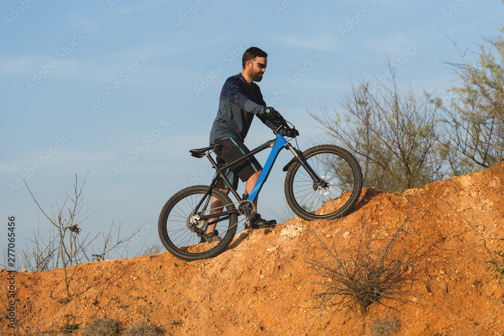 Naklejka premium Cyclist in shorts and jersey on a modern carbon hardtail bike with an air suspension fork rides off-road on the orange-red hills at sunset evening in summer 