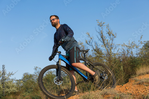 Cyclist in shorts and jersey on a modern carbon hardtail bike with an air suspension fork rides off-road on the orange-red hills at sunset evening in summer  © Mountains Hunter