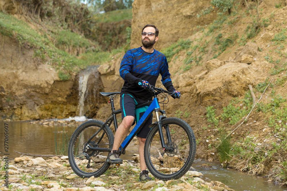 Fototapeta premium Cyclist in shorts and jersey on a modern carbon hardtail bike with an air suspension fork rides off-road on the orange-red hills at sunset evening in summer 