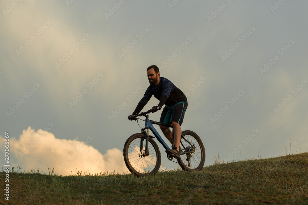 Fototapeta premium Cyclist in shorts and jersey on a modern carbon hardtail bike with an air suspension fork rides off-road on the orange-red hills at sunset evening in summer 
