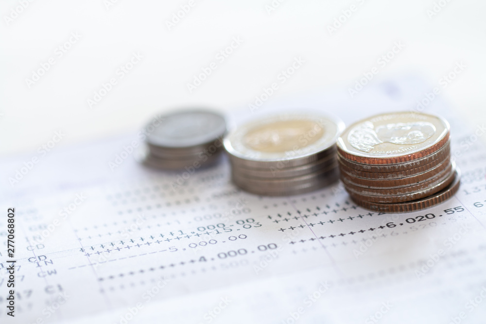 Selective focus of Thai's coins stacked over page of Bank account statement on white background, Collecting money for investment concept with copy space Selective focus of Thai's coins stacked over page of Bank account statement on white background, Collecting money for investment concept with copy space