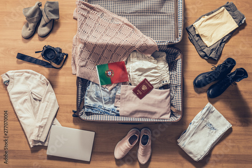 Woman's clothes, laptop, camera, russian passport and flag of Portugal lying on the parquet floor near and in the open suitcase. Travel concept