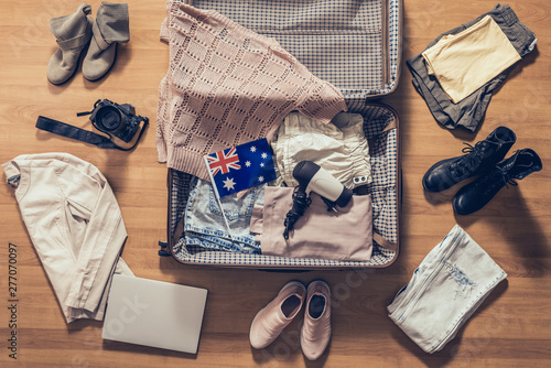 Woman's clothes, laptop, camera and flag of Australia lying on the parquet floor near and in the open suitcase. Travel concept