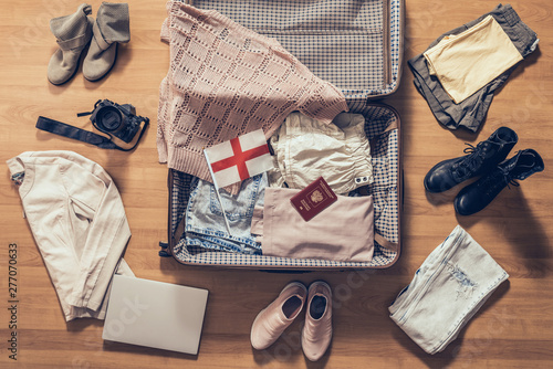 Woman's clothes, laptop, camera, russian passport and flag of England lying on the parquet floor near and in the open suitcase. Travel concept