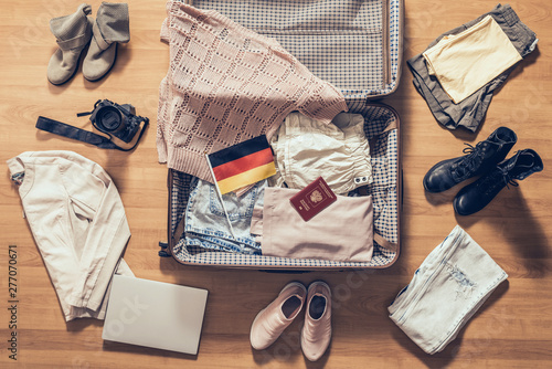 Woman's clothes, laptop, camera, russian passport and flag of Germany lying on the parquet floor near and in the open suitcase. Travel concept
