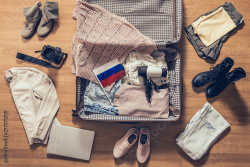 Woman's clothes, laptop, camera and flag lying on the parquet floor near and in the open suitcase. Travel concept