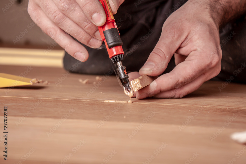 Handwerker bessert Fehlstellen im Parkett mit Reperaturset aus Handwerker bessert Fehlstellen im Parkett mit Reperaturset aus