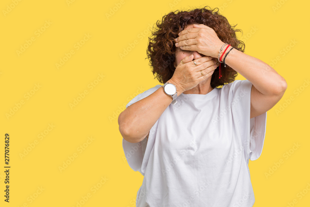 Beautiful middle ager senior woman wearing white t-shirt over isolated background Covering eyes and mouth with hands, surprised and shocked. Hiding emotion Beautiful middle ager senior woman wearing white t-shirt over isolated background Covering eyes and mouth with hands, surprised and shocked. Hiding emotion