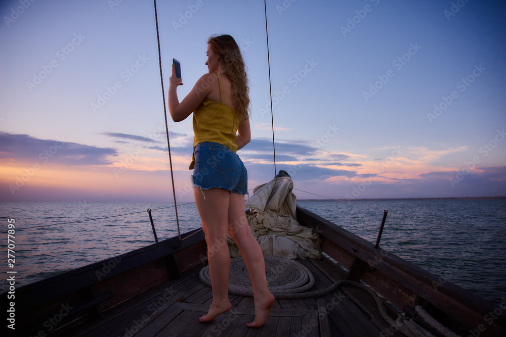 Girl takes a photo of sunset. Young woman meets sunrise on boat